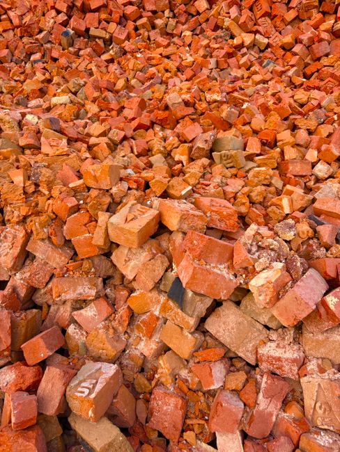 A large pile of debris consisting of twisted metal, broken structural components, and assorted discarded furniture is situated in front of a partially constructed or damaged commercial building. The d